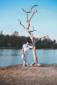 Man standing on tree by lake against sky