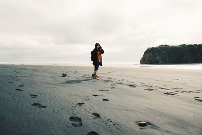 Woman standing on beach against cloudy sky