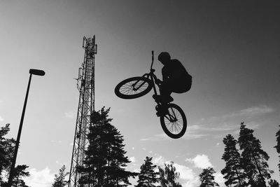 Low angle view of silhouette man jumping with bicycle against sky