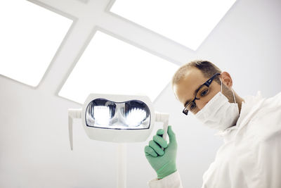 Low angle view of dentist adjusting lamp in clinic