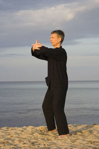 Man practicing tai chi at beach against cloudy sky