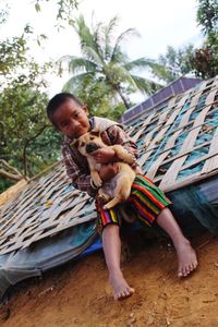 Portrait of boy holding puppy while sitting on seat against trees