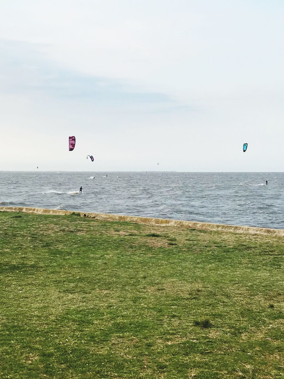 sea, sky, water, horizon over water, extreme sports, adventure, land, sport, beauty in nature, scenics - nature, horizon, parachute, nature, day, paragliding, grass, unrecognizable person, leisure activity, tranquility, outdoors, kiteboarding