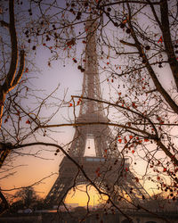 Low angle view of eiffel tower seen through bare tree against sky at sunset