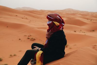 Side view of woman with headscarf sitting on sand dune