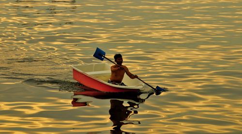 Shirtless mature man rowing rowboat in lake at sunset