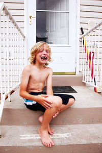 Boy crying in pain while sitting on steps outside house