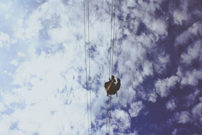 Directly below view of a person using aerial lift against cloudy sky