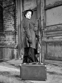Portrait of woman with suitcase standing on doorway