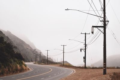 Road by electricity pylon against sky