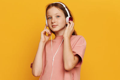 Young woman listening music against yellow background