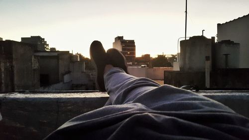 Low section of man with cityscape against sky during sunset