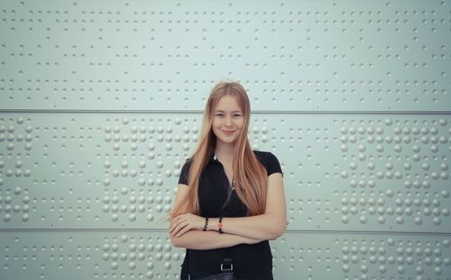 Young woman holding camera while standing against wall