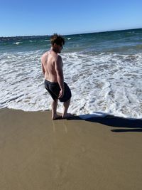 Full length of shirtless man at beach against sky