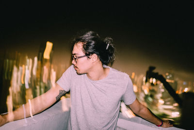 Man looking away while standing on terrace against illuminated city at night