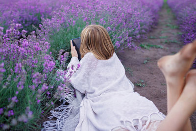 Teenage girl enjoys lavender field, makes photo with smartphone. summer travel, vacation, back view