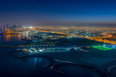 High angle view of illuminated city by sea against sky at night