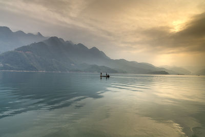 People on lake against sky during sunset