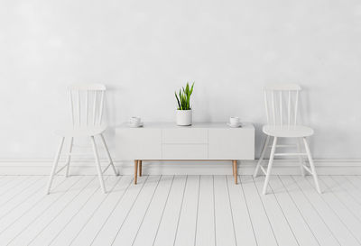 Empty chairs and table against white wall