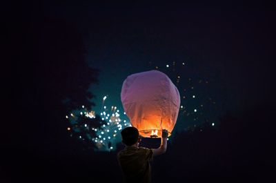 Rear view of boy holding illuminated lantern at night