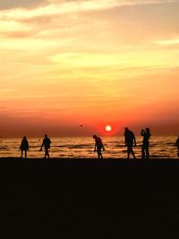 Silhouette people on beach against sky during sunset