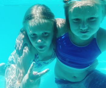 Portrait of girl with sister showing peace sign in swimming pool