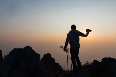 Rear view of man photographing on rock against sky