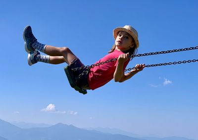 Side view portrait of boy on swing against blue sky