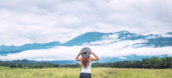 Rear view of woman with arms outstretched standing on field against sky