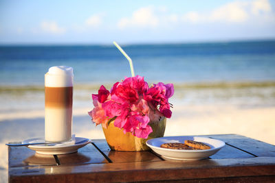 Close-up of late machiatto and coconut drink on table against sea