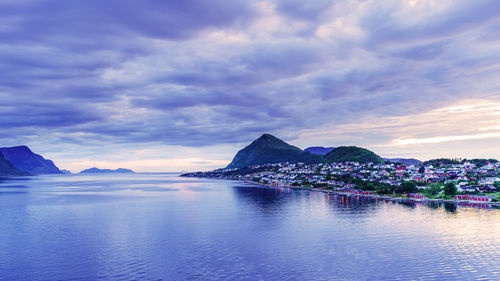 Scenic view of sea by houses against cloudy sky during sunset