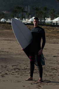 Portrait of man holding surfboard while standing at beach