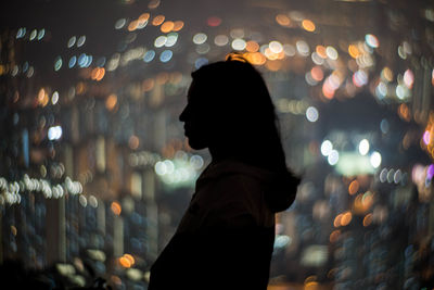 Side view of woman standing against defocused lights