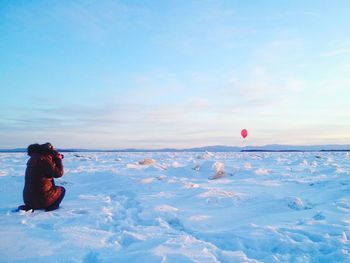 Rear view of person photographing helium balloon over snow covered field