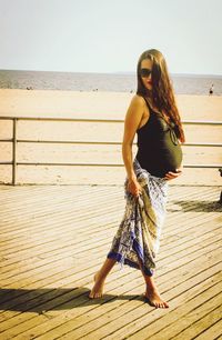Pregnant woman standing on deck at beach