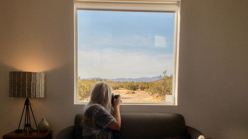 Rear view of woman photographing while sitting on sofa at home