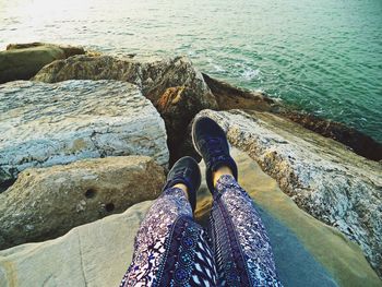 Low section of woman standing on rock by sea