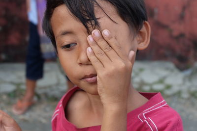 Close-up of cute boy with hand on face looking away while standing outdoors