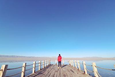 Rear view of man standing on railing against clear blue sky