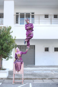 Digital composite image of bride lifting groom while sitting against building