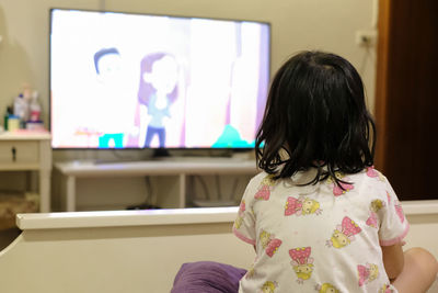 Rear view of girl sitting at home