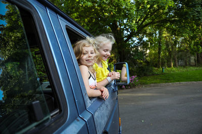 Two young girls smiling and leaning out of car window