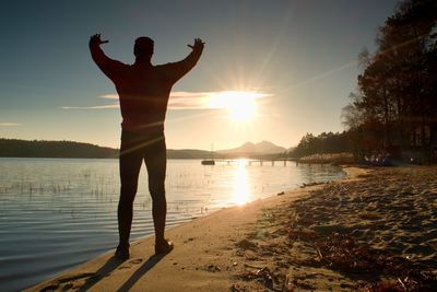 Slim sportsman on beach shadowing eyes and looks into sun