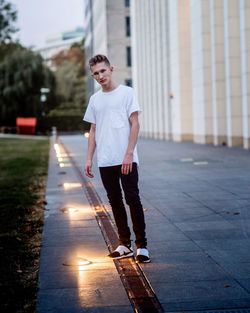 Portrait of young man standing by illuminated recessed lights on footpath
