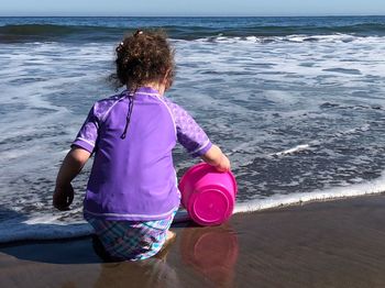Rear view of girl with bucket playing at beach