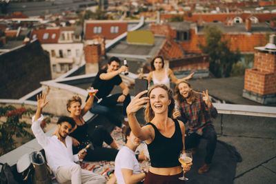 Woman having drink while taking selfie with friends on smart phone at terrace in party