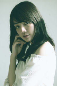 Close-up portrait of young woman standing against white background