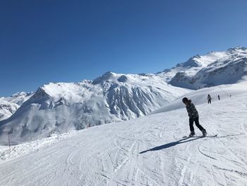 Woman snowboarding on snowcapped mountain against clear sky