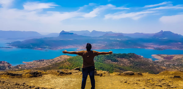 Rear view of man with arms outstretched standing on mountain against sky