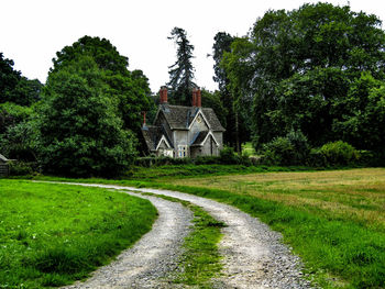 Scenic view of field by trees and houses against sky